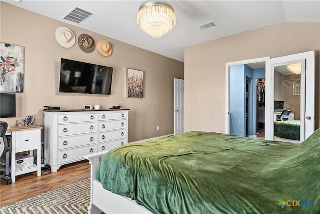 bedroom featuring a notable chandelier, visible vents, lofted ceiling, and wood finished floors