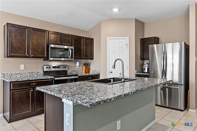 kitchen with a sink, stainless steel appliances, dark brown cabinetry, light tile patterned floors, and light stone countertops