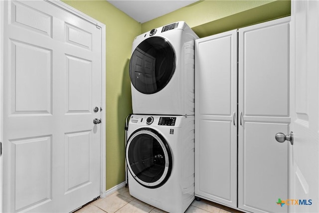 laundry area with stacked washer / dryer, light tile patterned flooring, cabinet space, and baseboards