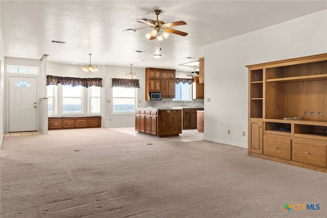 unfurnished living room with light carpet, sink, ceiling fan with notable chandelier, and a textured ceiling