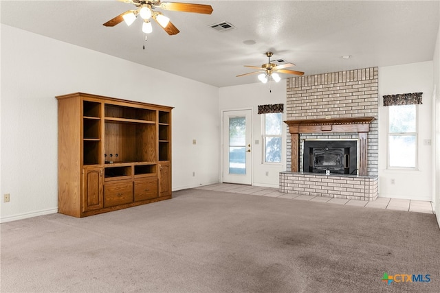 unfurnished living room with a wood stove, light carpet, and ceiling fan