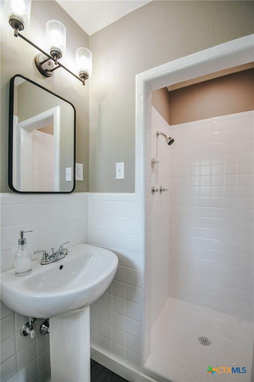 full bathroom with tile walls, a stall shower, and wainscoting