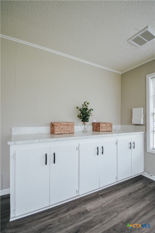 interior space featuring visible vents, ornamental molding, a textured ceiling, and wood finished floors