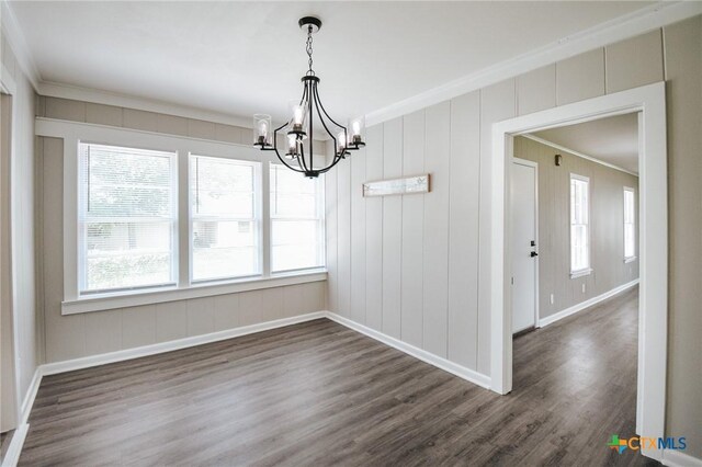 unfurnished dining area with a notable chandelier, baseboards, dark wood-type flooring, and crown molding