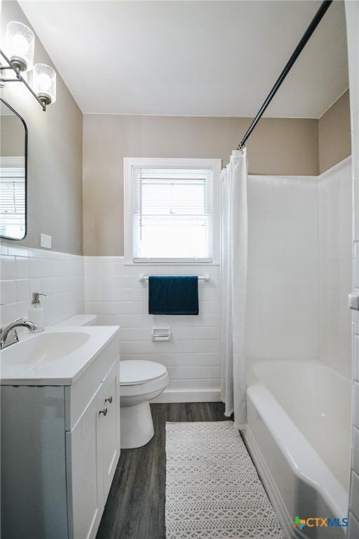 full bathroom with vanity, shower / bathtub combination with curtain, wood finished floors, tile walls, and toilet