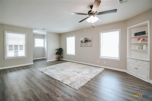 spare room featuring visible vents, built in shelves, baseboards, and dark wood-style flooring