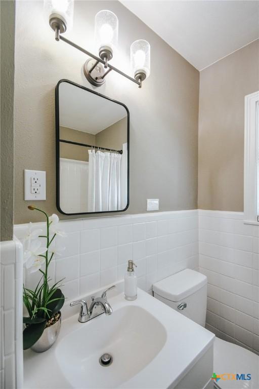 full bathroom featuring wainscoting, toilet, tile walls, and a sink