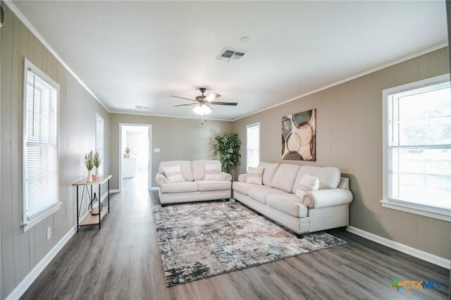 living area with a wealth of natural light, visible vents, wood finished floors, and ornamental molding