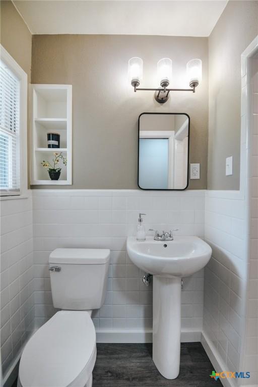 half bath featuring a wainscoted wall, toilet, tile walls, and wood finished floors