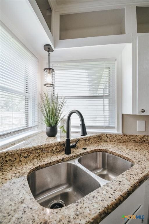 interior details featuring hanging light fixtures, white cabinets, light stone countertops, and a sink