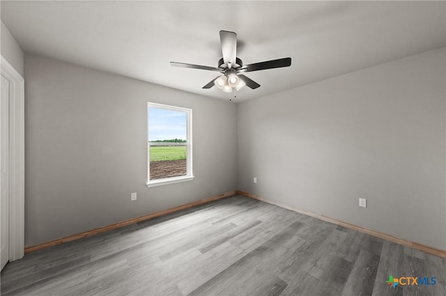 empty room with a ceiling fan, wood finished floors, and baseboards