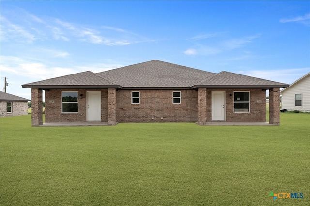 rear view of property featuring a patio, a yard, a shingled roof, and brick siding