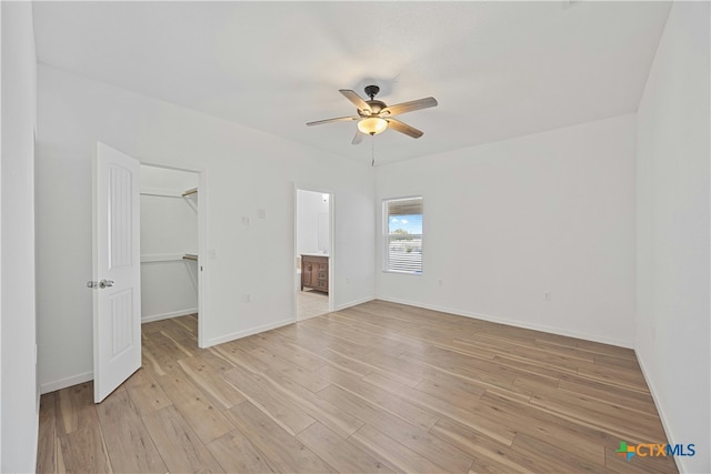 unfurnished bedroom featuring connected bathroom, light hardwood / wood-style flooring, a spacious closet, ceiling fan, and a closet