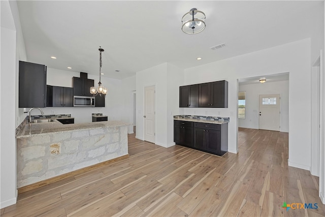 kitchen with sink, kitchen peninsula, pendant lighting, light stone countertops, and light hardwood / wood-style floors