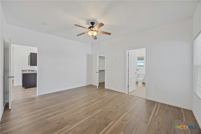 unfurnished bedroom featuring ensuite bathroom, a spacious closet, light wood-type flooring, a closet, and ceiling fan