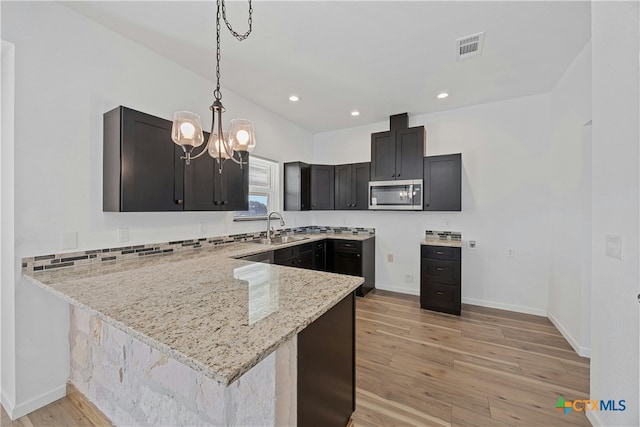 kitchen featuring sink, light stone counters, hanging light fixtures, light hardwood / wood-style flooring, and kitchen peninsula