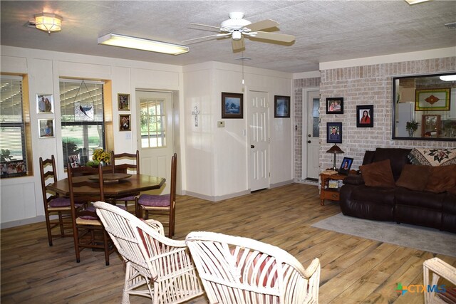 living room with a textured ceiling, wood-type flooring, ceiling fan, and brick wall