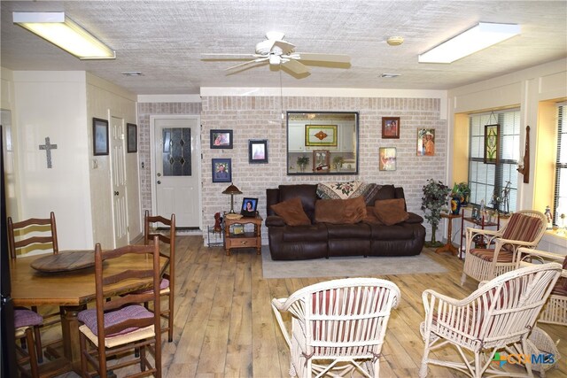 living room featuring ceiling fan, a textured ceiling, brick wall, and light hardwood / wood-style flooring