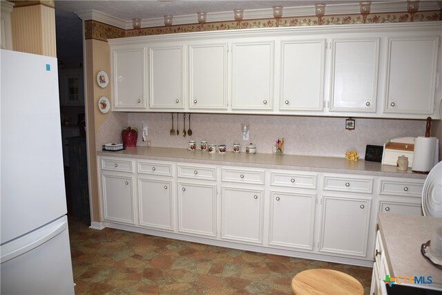 kitchen with backsplash, white refrigerator, ornamental molding, and white cabinets