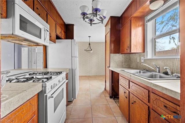 kitchen featuring a textured ceiling, white appliances, sink, light tile patterned floors, and an inviting chandelier