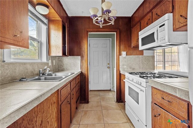 kitchen with decorative backsplash, white appliances, sink, light tile patterned floors, and a notable chandelier