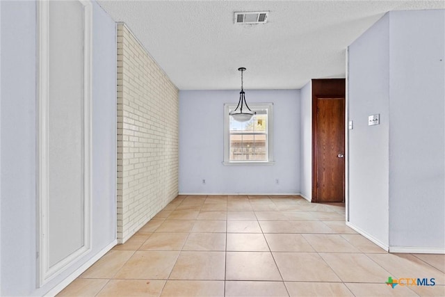 unfurnished dining area with light tile patterned floors, brick wall, and a textured ceiling