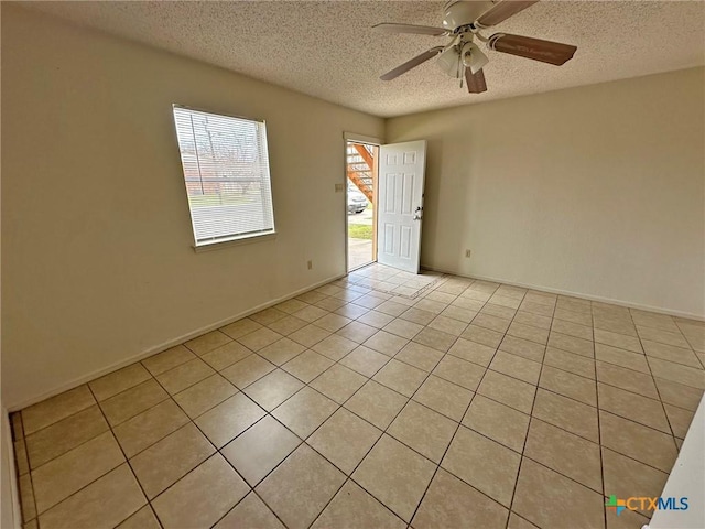 spare room featuring a textured ceiling, ceiling fan, light tile patterned flooring, and baseboards