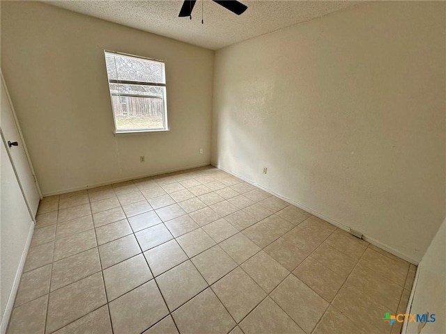 empty room with a textured ceiling, light tile patterned floors, a ceiling fan, and baseboards