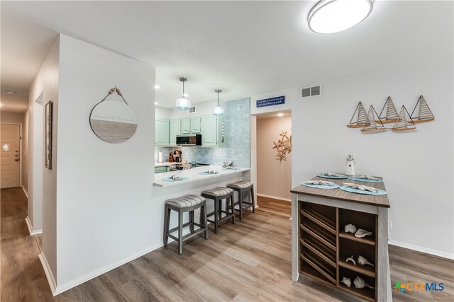 kitchen with green cabinets, a breakfast bar, kitchen peninsula, hardwood / wood-style floors, and decorative backsplash