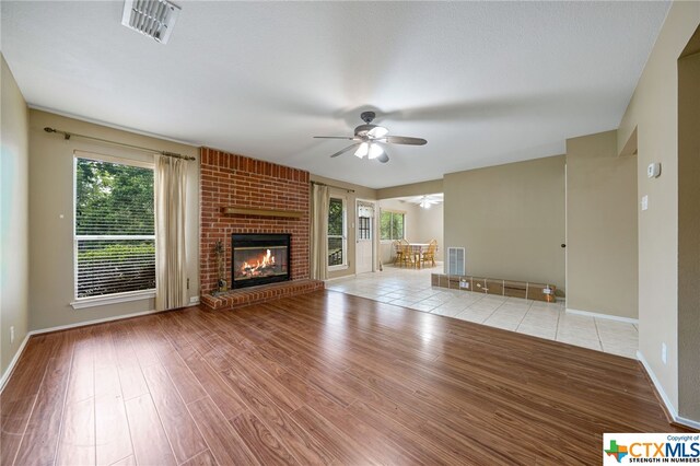 unfurnished living room with a fireplace, ceiling fan, a healthy amount of sunlight, and light hardwood / wood-style flooring