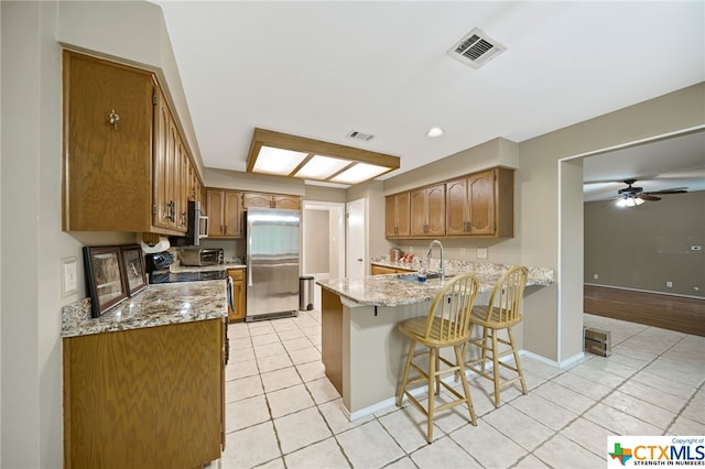 kitchen featuring stainless steel appliances, light stone counters, kitchen peninsula, ceiling fan, and a breakfast bar area