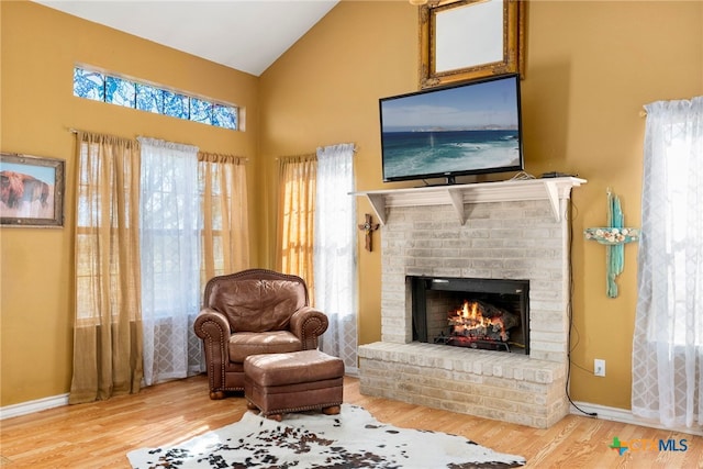 sitting room featuring a fireplace, high vaulted ceiling, a healthy amount of sunlight, and light wood-type flooring