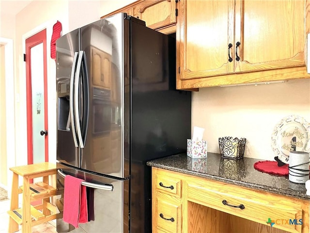 kitchen featuring dark stone counters and stainless steel refrigerator with ice dispenser