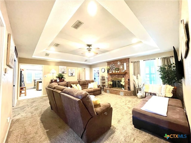 living area with a tray ceiling, visible vents, a ceiling fan, and carpet flooring