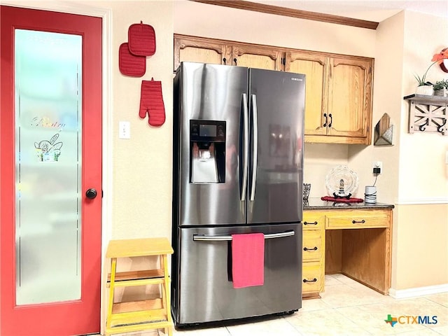 kitchen featuring light tile patterned floors, baseboards, brown cabinets, dark countertops, and stainless steel fridge