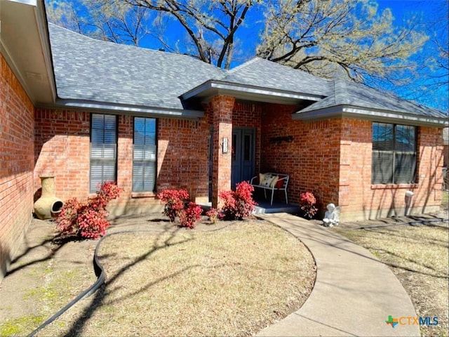 exterior space featuring brick siding and a shingled roof