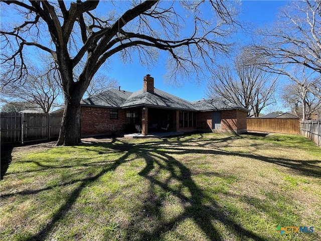 back of property with brick siding, a fenced backyard, a chimney, and a yard