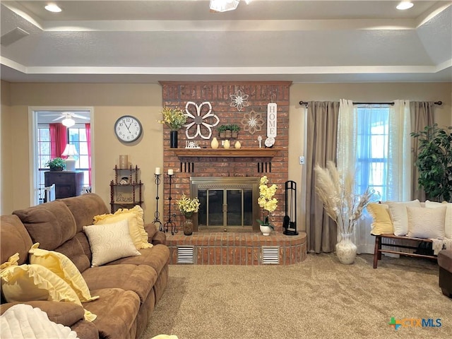 carpeted living area featuring a fireplace, a raised ceiling, a healthy amount of sunlight, and visible vents