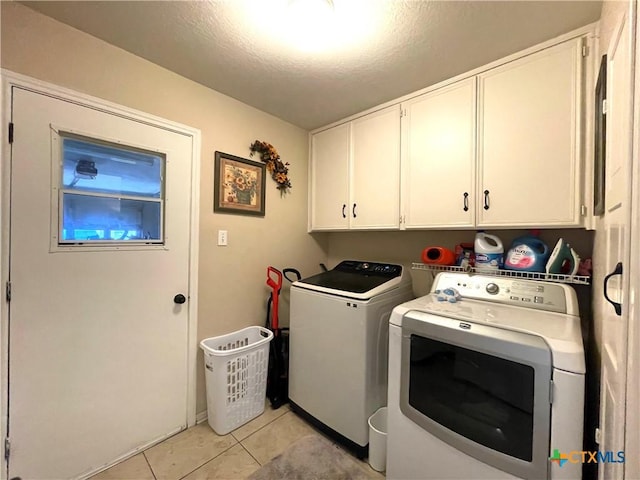 laundry room with washing machine and dryer, light tile patterned flooring, cabinet space, and a textured ceiling