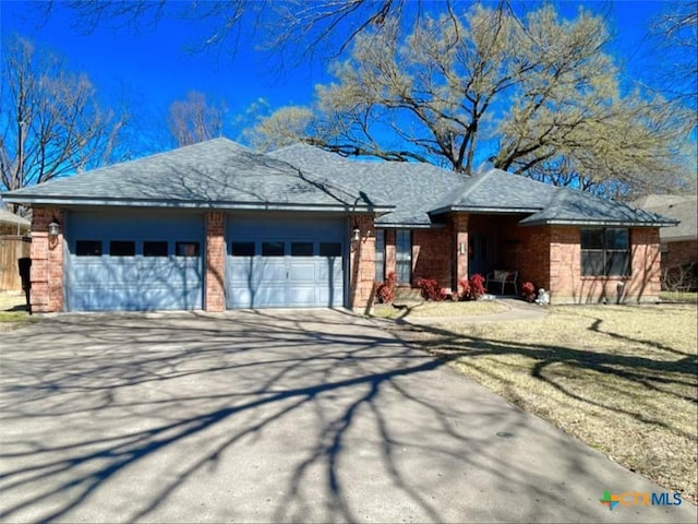 single story home featuring brick siding, concrete driveway, a garage, and roof with shingles