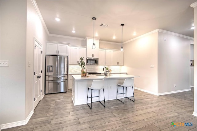 kitchen with appliances with stainless steel finishes, decorative light fixtures, a center island with sink, and white cabinets