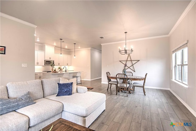 living room featuring a notable chandelier, crown molding, wood-type flooring, and sink