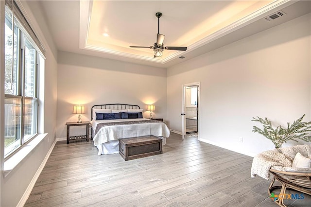 bedroom with ceiling fan, a raised ceiling, multiple windows, and light wood-type flooring