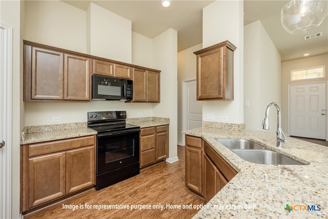 kitchen featuring light hardwood / wood-style floors, light stone counters, hanging light fixtures, black appliances, and sink