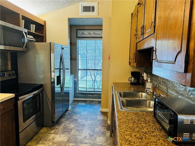 505 Cabana Dr, Victoria, TX 77901 - kitchen featuring appliances with stainless steel finishes, a sink, a textured ceiling, brown cabinetry, and vaulted ceiling