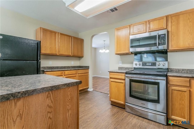 kitchen featuring arched walkways, dark countertops, appliances with stainless steel finishes, wood finished floors, and baseboards