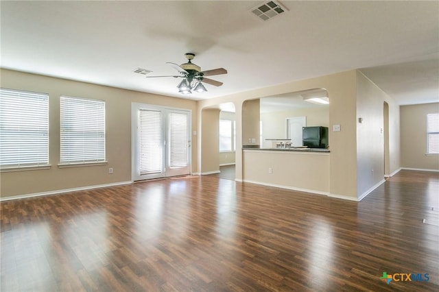 unfurnished living room with arched walkways, dark wood-style flooring, visible vents, and a ceiling fan