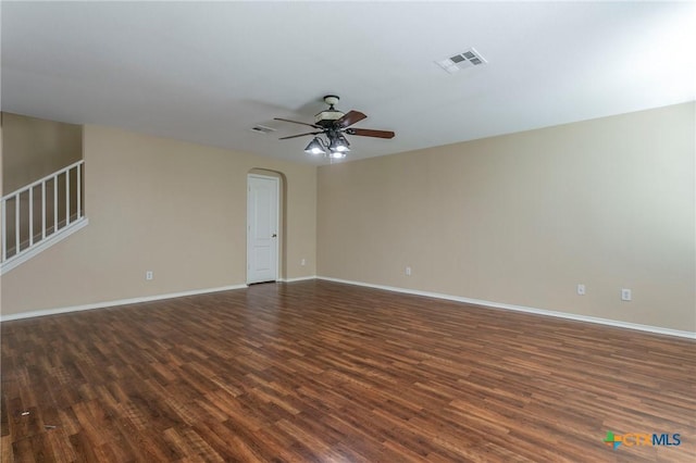 spare room featuring arched walkways, a ceiling fan, baseboards, stairs, and dark wood finished floors