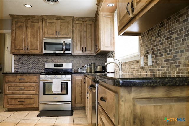 kitchen with dark stone counters, appliances with stainless steel finishes, decorative backsplash, and light tile patterned floors