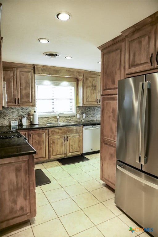 kitchen with tasteful backsplash, appliances with stainless steel finishes, light tile patterned floors, sink, and dark stone countertops